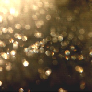 May include: An abstract image with a blurred focus, showing many golden, circular bokeh lights against a dark background. The lights vary in size and intensity, creating a shimmering, ethereal effect. The overall impression is one of warmth and radiance.