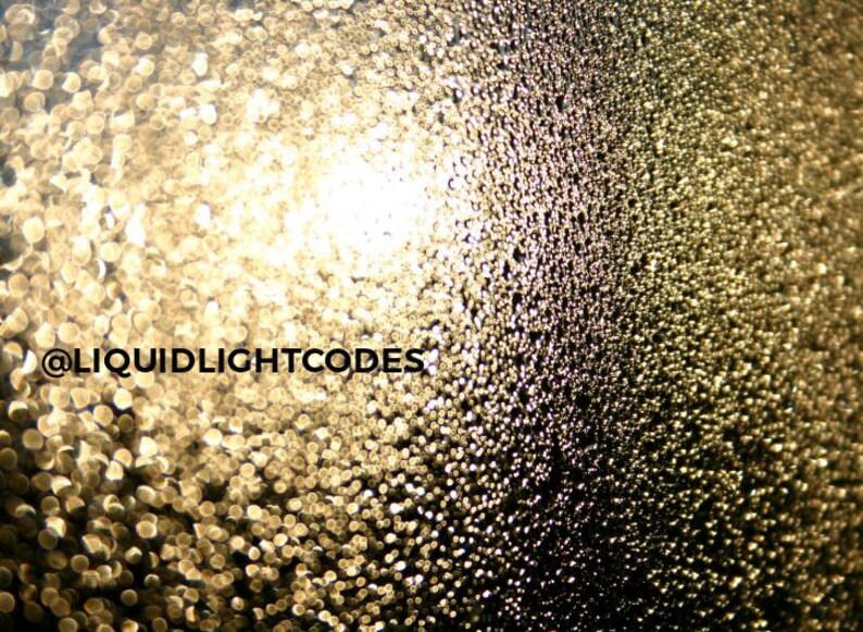 K&ouml;nnte beinhalten: Abstraktes Bild mit Bokeh-Effekt, das einen Farbverlauf von Gold- und dunklen T&ouml;nen aufweist. Das Bild hat einen verschwommenen Hintergrund mit kleinen, kreisf&ouml;rmigen Lichtreflexen. Der Text lautet "@LIQUIDLIGHTCODES".