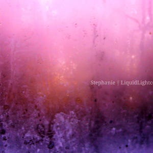 以下が含まれることがあります： ピンク、紫、オレンジの色合いのグラデーションが特徴的な抽象的なデジタルアート。 画像はテクスチャ加工が施されており、黒い斑点があり、右下に「Stephanie | LiquidLightcodes」というテキストがあります。