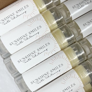 May include: A close-up of several white tubes with a gold sunburst design and the text "SUNSHINE SMILES Teeth Whitening" on the label. The tubes are filled with a white substance.