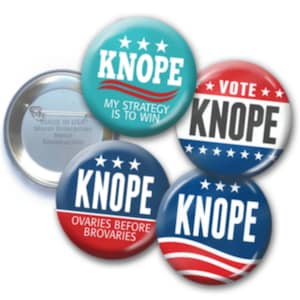 May include: Four round campaign buttons with the name "KNOPE" printed on them. The buttons have different colors and slogans. One button is blue with white stars and the slogan "VOTE". Another button is blue with white stars and the slogan "OVARIES BEFORE BROVARIES". Another button is turquoise with white stars and the slogan "MY STRATEGY IS TO WIN". The last button is blue with red and white stripes and the slogan "KNOPE".