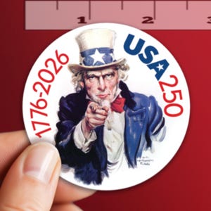 May include: A white ceramic mug with a black handle and the text "But First, Coffee" in a bold, black font. The mug is set against a blurred background, suggesting a cozy setting.