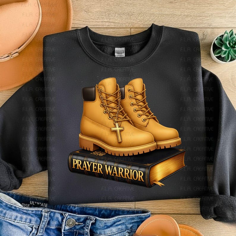 A black sweatshirt with a graphic design of yellow boots and a book titled "Prayer Warrior" printed on it, along with a cross.