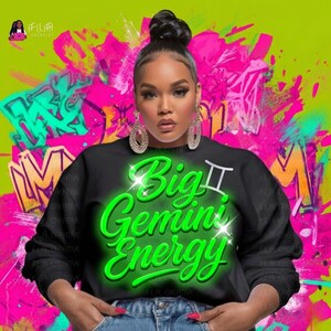 Op de afbeelding: Een zwarte sweatshirt met de tekst "Big Gemini Energy" in felgroen, met een Tweeling-symbool. De achtergrond heeft graffiti-kunst in roze, groen en oranje. De afbeelding toont een vrouw die de sweatshirt draagt.