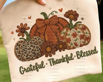 May include: A beige fabric item featuring a fall-themed design. The design includes three pumpkins with different patterns, brown flowers, and the text "Grateful Thankful Blessed" in green. Decorative hearts and stars are also present.