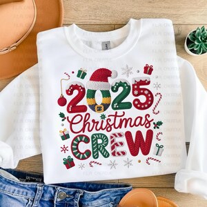 A white t-shirt with a Christmas-themed design, including the text "2025 Christmas Crew" and various holiday-related elements such as snowflakes, presents, and a Santa hat.