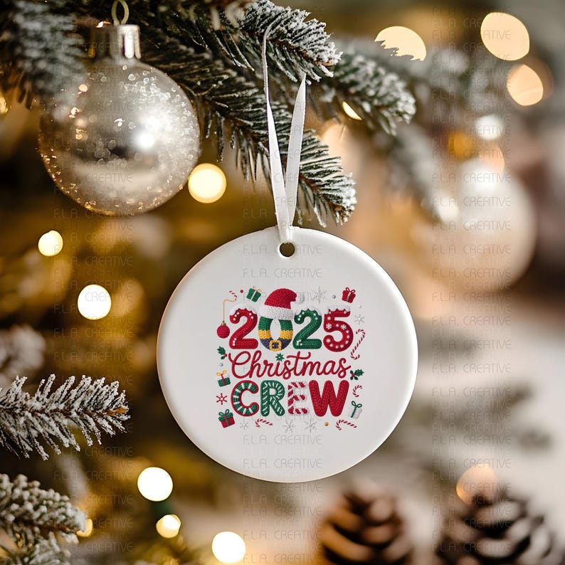 A white ornament with the text "2025 Christmas Crew" is hanging on a Christmas tree, surrounded by other ornaments and lights.