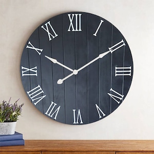 May include: A large, round, black clock with white Roman numeral markings and silver hands. The clock face has a wood plank design.