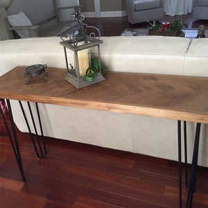 May include: A wooden console table with a chevron pattern top and black hairpin legs. The table is decorated with a lantern and a small decorative object.