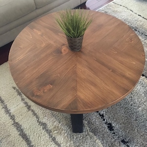 May include: A round wooden coffee table with a chevron pattern top and black metal legs. A small potted plant sits on the table.