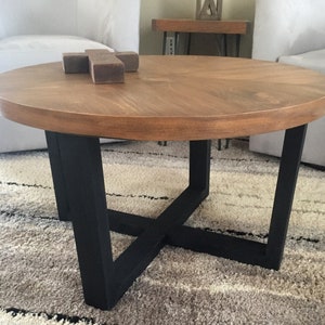 May include: A round wooden coffee table with a black metal base. The table has a natural wood finish and a simple, modern design.