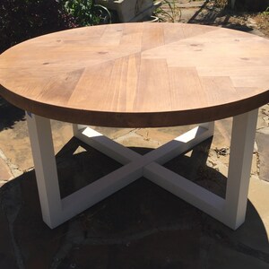 May include: Round wooden table with a white, cross-shaped base. The table top has a chevron pattern.