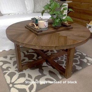 May include: A round wooden coffee table with a chevron pattern on the top. The table has a cross-shaped base with stained legs. The table is sitting on a patterned rug. "Stained legs instead of black" is written on the rug.