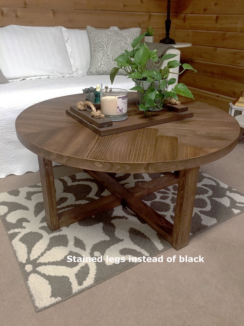 May include: A round wooden coffee table with a chevron pattern on the top. The table has a cross-shaped base with stained legs. The table is sitting on a patterned rug. "Stained legs instead of black" is written on the rug.
