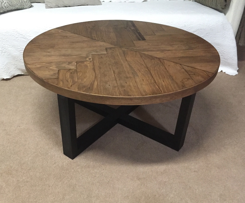 May include: Round wooden coffee table with a chevron pattern top and black metal legs.