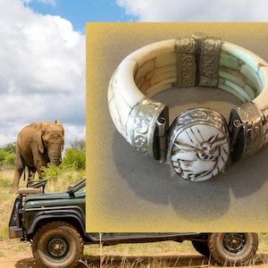 May include: A white and silver bangle bracelet with an intricate design. The bracelet is made of bone and metal and has a clasp closure.