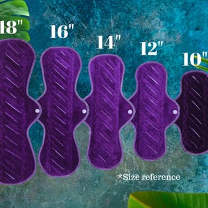 Five purple reusable cloth menstrual pads, sizes from 25.4 cm to 45.7 cm in length. Each pad has a quilted design and white stitching. The text "*Size reference" is at the bottom.