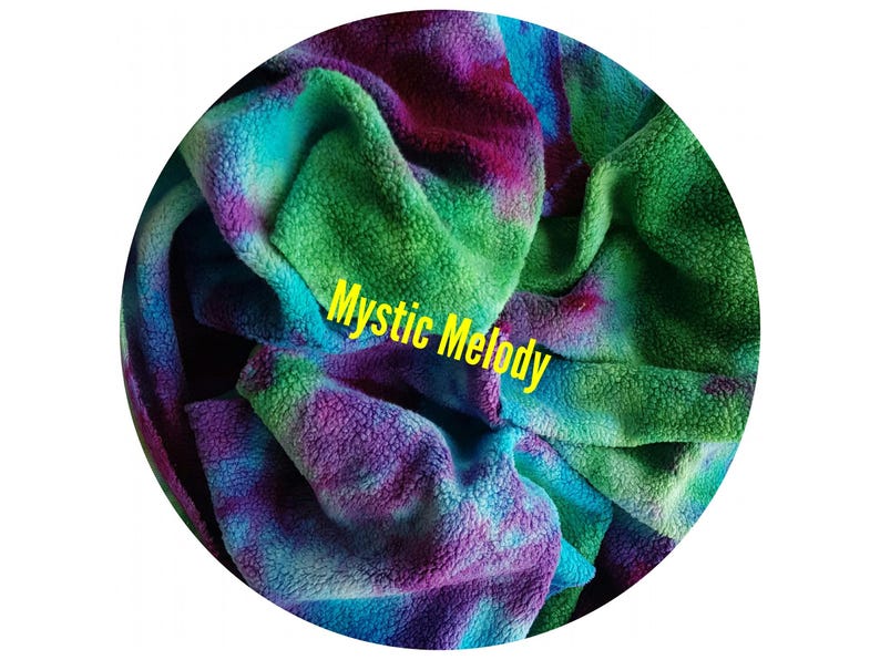May include: A soft, tie-dye fleece fabric in a circular shape. The cotton sherpa fabric features vibrant colours of green, blue, and purple. The text "Mystic Melody" is displayed in yellow across the organic cotton sherpa fleece fabric. This fabric swatch is an option for custom made organic cotton sherpa gusher pads.