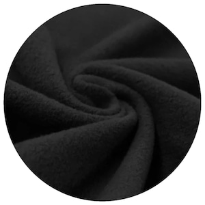 Close-up of black organic cotton sherpa fleece fabric, displaying its soft texture and folds. The material appears thick and warm, suitable for clothing or cloth menstrul pads. The image is set against a black background.