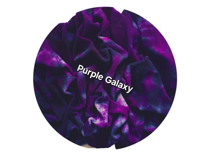 Organic cotton sherpa fabric with a tie-dye design in shades of purple and dark blue. The words "Purple Galaxy" are printed across the center in white. The blanket appears to be made of a plush material, ideal for comfort.