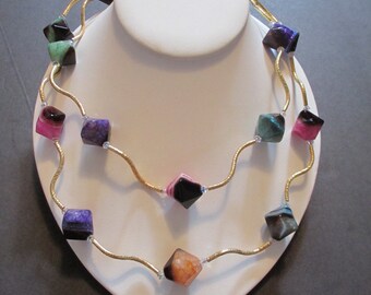 Puede incluir: Un collar de cadena dorada con una doble hilera de cuentas de piedra preciosa de ágata de colores. Las cuentas están cortadas en forma cuadrada y tienen una variedad de colores, incluyendo rosa, verde, morado y negro.