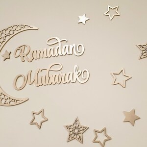May include: A wooden crescent moon with intricate cutouts and the words "Ramadan Mubarak" in a decorative script, surrounded by wooden stars of various designs.