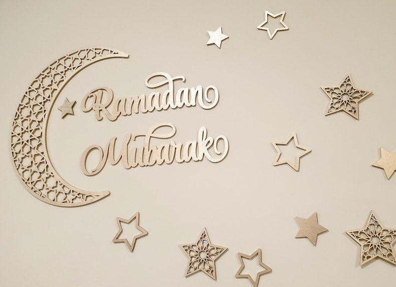 May include: A wooden crescent moon with intricate cutouts and the words "Ramadan Mubarak" in a decorative script, surrounded by wooden stars of various designs.
