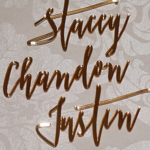 May include: Gold mirror acrylic names for a wedding or event. The names are Stacy, Chadon, and Justin.