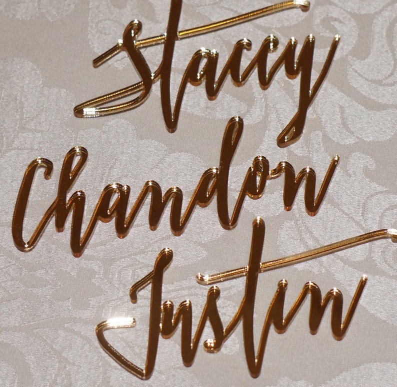 May include: Gold mirror acrylic names for a wedding or event. The names are Stacy, Chadon, and Justin.