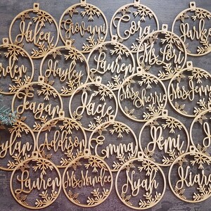 May include: A set of 18 wooden Christmas ornaments with snowflake designs and personalized names, including "Hakea", "Giovanni", "Coral", "Parker", "Erden", "Hayley", "Lauren", "Ms Lori", "Leagan", "Kacie", "Miss Sherrie", "Mrs Jenny", "Dylan", "Addison", "Emma", "Remi", "Hal", "Lauren", "Ms Mandee", "Nyah", and "Kiara".