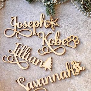 Op de afbeelding: Vijf houten kerstversieringen met namen in cursief schrift. De namen zijn Joseph, Kobe, Lillian, Savannah en een gingerbread man versiering.