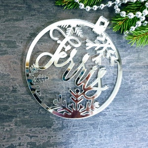 May include: Silver mirrored Christmas ornament with the word "Merry" cut out and snowflake designs around the edge.