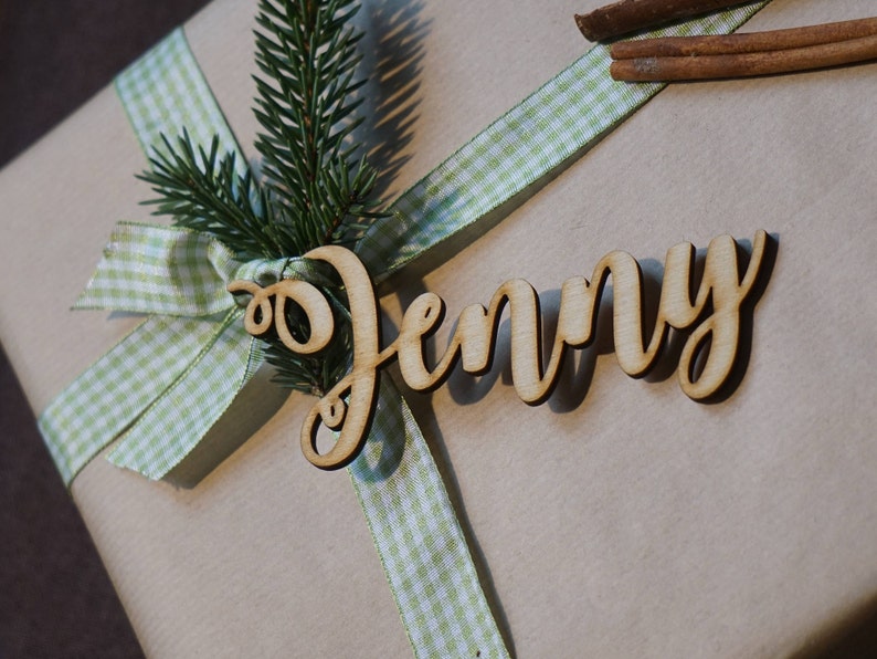Puede incluir: Una caja de regalo marr&oacute;n con una cinta de cuadros verdes y blancos y una etiqueta de madera que dice "Jenny".