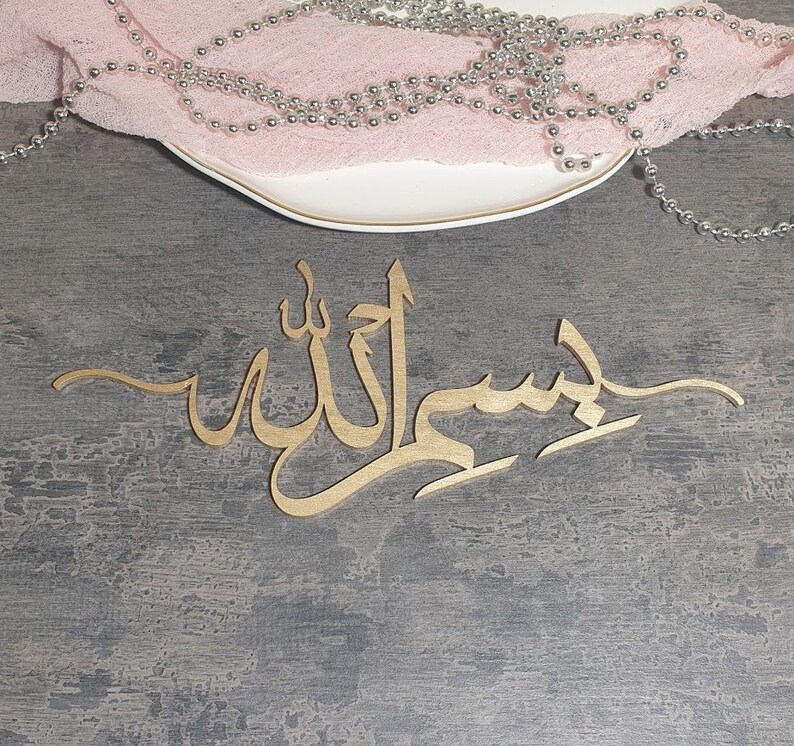 Op de afbeelding: Gouden kalligrafie wanddecoratie met het Arabische woord "Insha'Allah" op een grijze achtergrond.