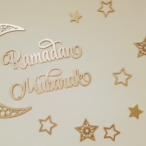 May include: A wooden crescent moon with intricate cutouts and the words "Ramadan Mubarak" in a decorative script, surrounded by gold stars of various sizes and designs.