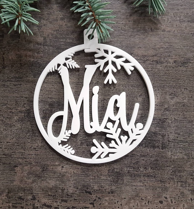 May include: White wooden Christmas ornament with a snowflake design and the name "Mia" cut out in the center.