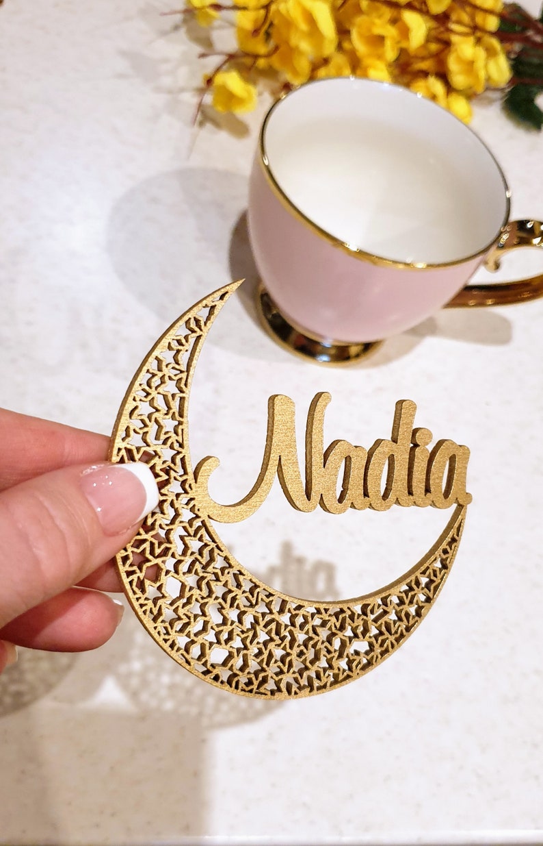 May include: A gold wooden crescent moon with a delicate star pattern and the name Nadia cut out in the center.