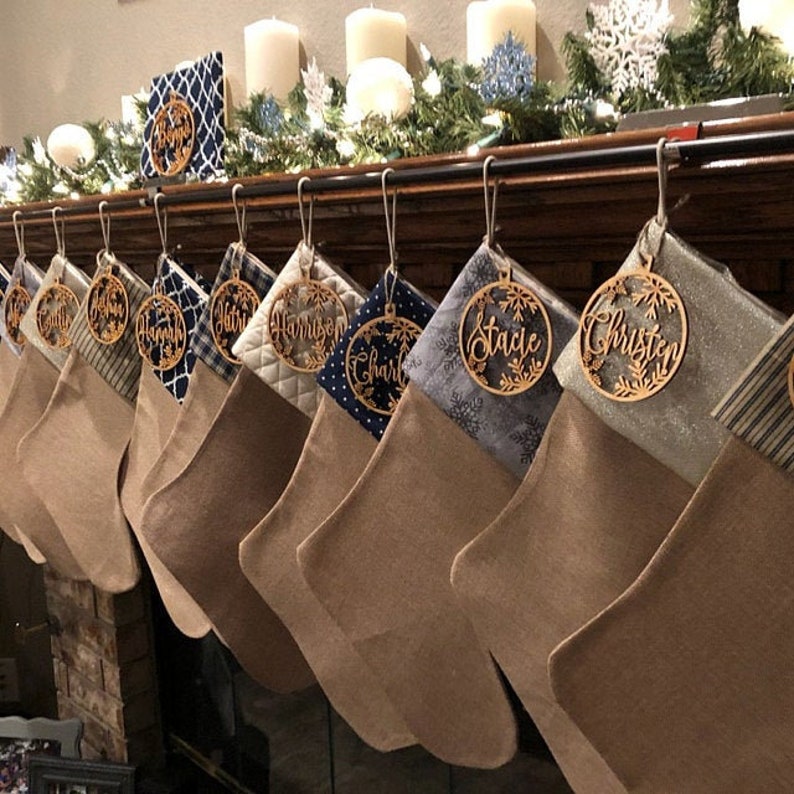 May include: A set of 10 personalized Christmas stockings with wooden ornaments featuring names like "Charlie", "Stacie", and "Harrison". The stockings are brown and the ornaments are a light wood color.