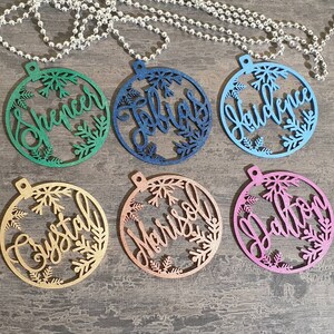 May include: Six round, wooden ornaments with snowflake designs and personalized names. The ornaments are painted in various colors, including green, blue, pink, gold, and copper.