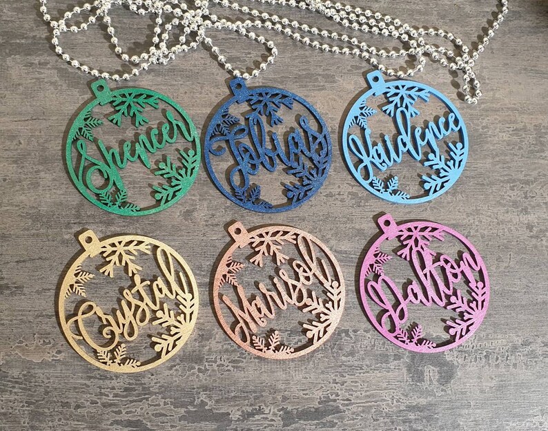 May include: Six round, wooden ornaments with snowflake designs and personalized names. The ornaments are painted in various colors, including green, blue, pink, gold, and copper.
