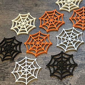 May include: Nine decorative spiderweb cutouts in three colours: black, white and orange. The cutouts are made of wood and have a simple, elegant design.