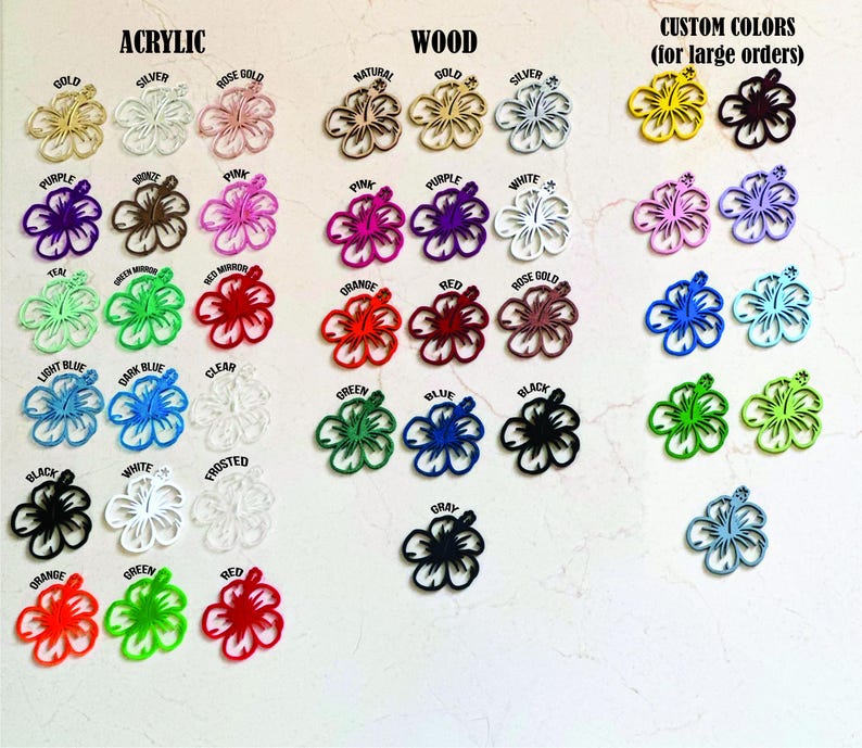 Puede incluir: Variedad de recortes de flores de hibisco en acr&iacute;lico y madera, disponibles en varios colores: oro, plata, rosa, morado, rojo, naranja, verde, azul y negro. Los textos "ACRYLIC", "WOOD" y "CUSTOM COLORS" est&aacute;n presentes.