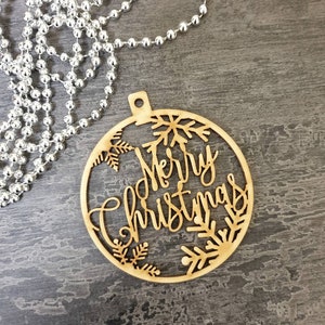 May include: A wooden Christmas ornament in the shape of a circle with the words "Merry Christmas" and snowflakes cut out.