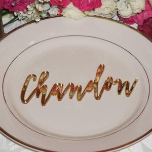 May include: Gold mirror acrylic table place card with the name "Chaydon" written in cursive.