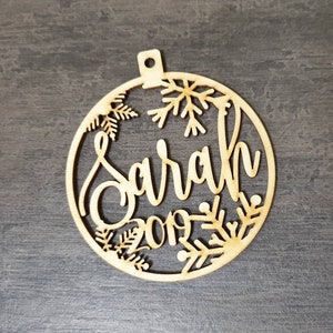 May include: A wooden Christmas ornament with a snowflake design and the name "Sarah" and the year "2019" cut out.