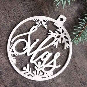 May include: White wooden Christmas ornament with a snowflake design and the word "Christmas" written in a cursive font.