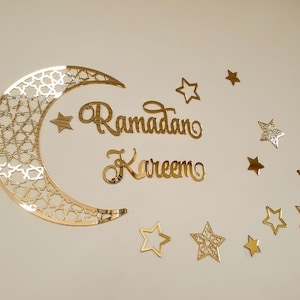 May include: Gold glitter Ramadan Kareem sign with a crescent moon and stars. The moon has a geometric pattern.