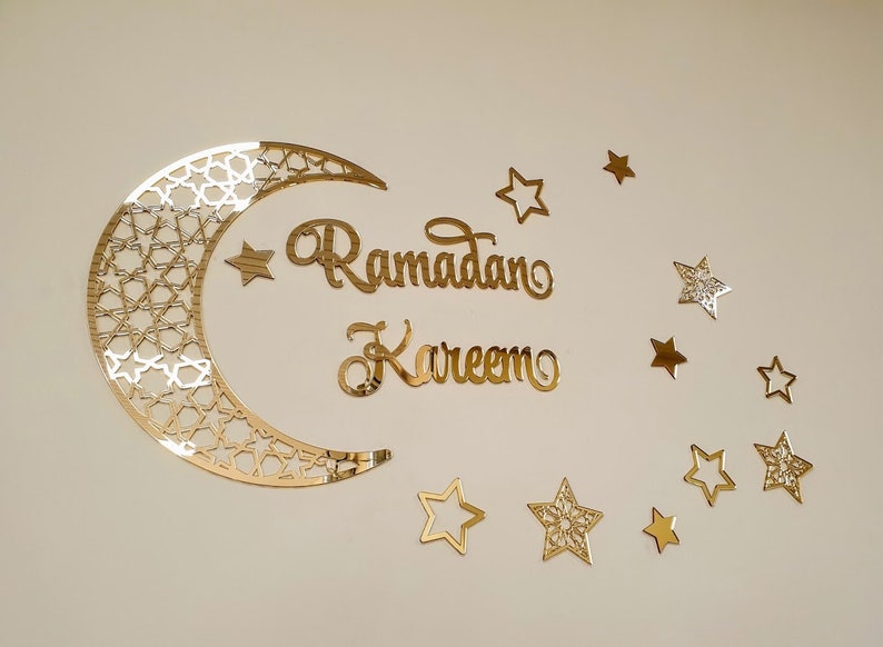 May include: Gold glitter Ramadan Kareem sign with a crescent moon and stars. The moon has a geometric pattern.