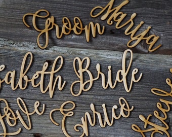 Puede incluir: Recortes de madera con las palabras "Groom", "Bride", "Marisa", "Elizabeth", "Enrico", "Love" y "Forever" en una fuente cursiva.