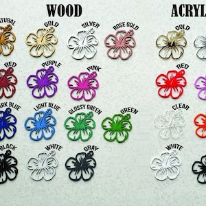 May include: Assortment of wooden and acrylic hibiscus flower embellishments in various colors, including natural, gold, silver, rose gold, red, purple, pink, dark blue, light blue, glossy green, green, clear, orange, black, white, and gray.